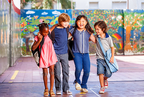 Four primary students arms linked in a playground with  bright mural on a wall behind them